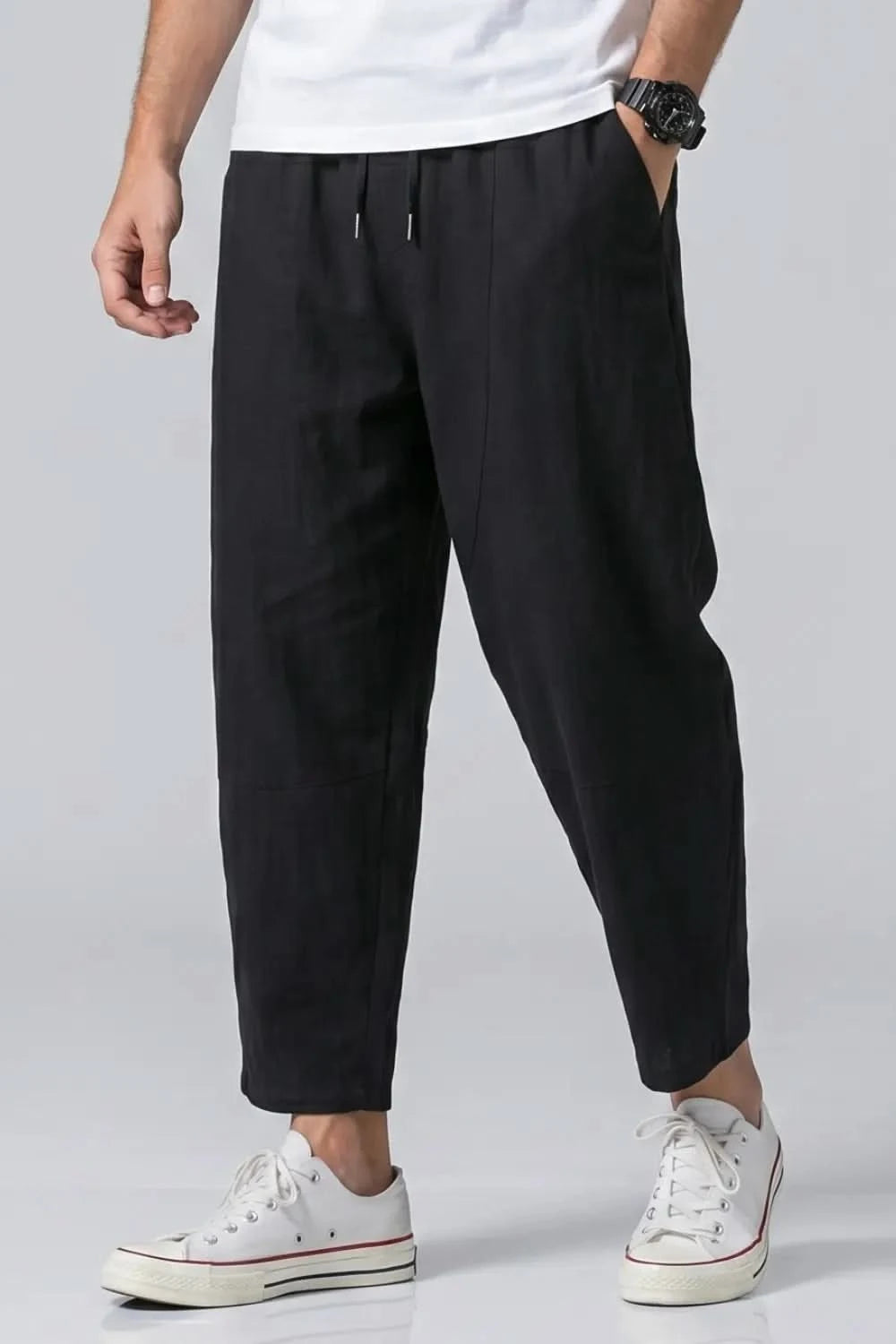 Person wearing black pants and white sneakers on a light gray background