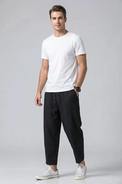 Man wearing a white t-shirt and black pants on a gray background