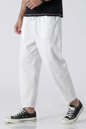 Person wearing white pants and black sneakers on a plain background