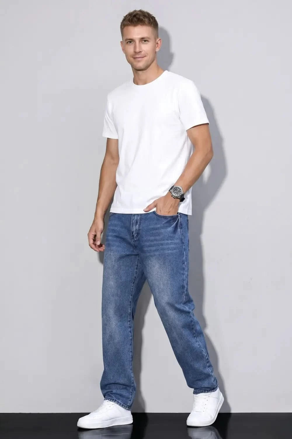 Man wearing a white t-shirt and blue jeans against a plain background