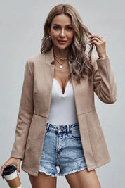 Woman wearing a beige blazer, white top, and denim shorts, holding a coffee cup.
