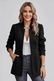 Woman wearing a black coat over a white top and gray pants on a plain background