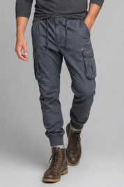 Person wearing dark gray cargo pants and brown boots on a plain background
