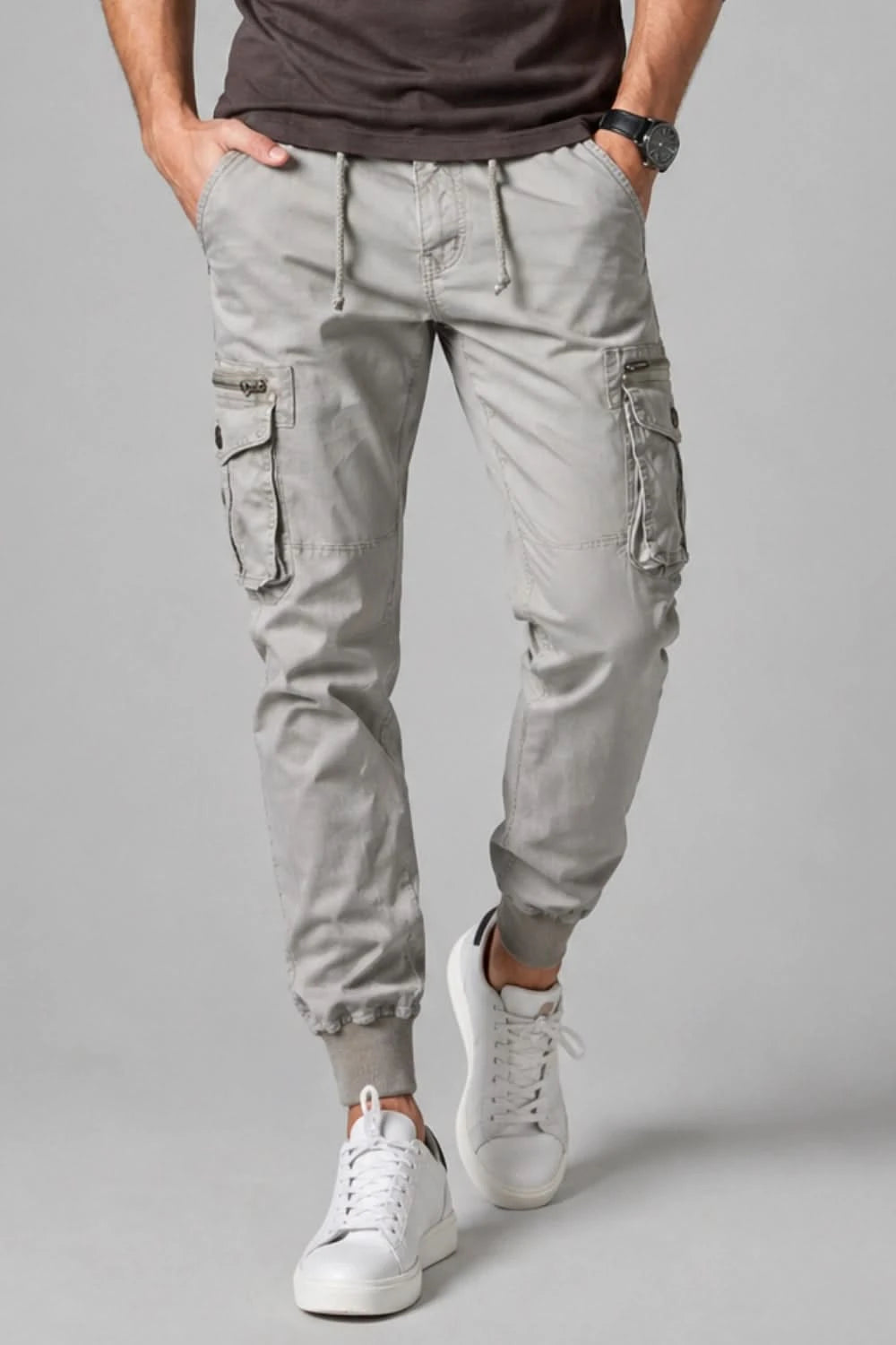 Person wearing light gray cargo pants and white sneakers on a gray background