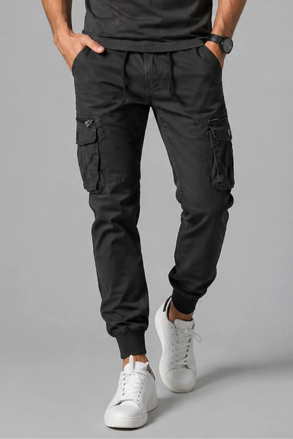 Person wearing black cargo pants and white sneakers on a gray background